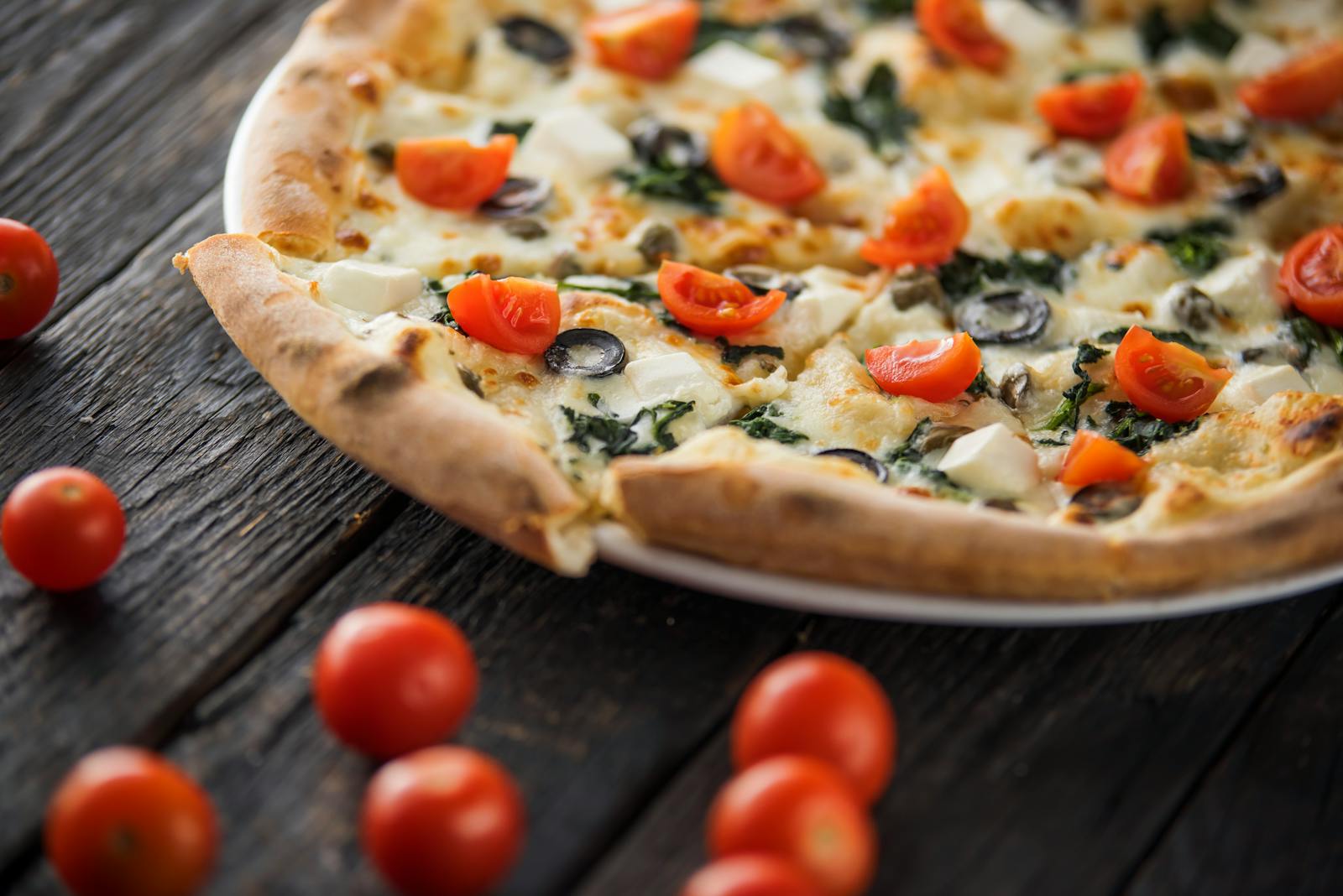 Tasty pizza slices with fresh tomatoes and black olive rings with soft cheese on wooden table