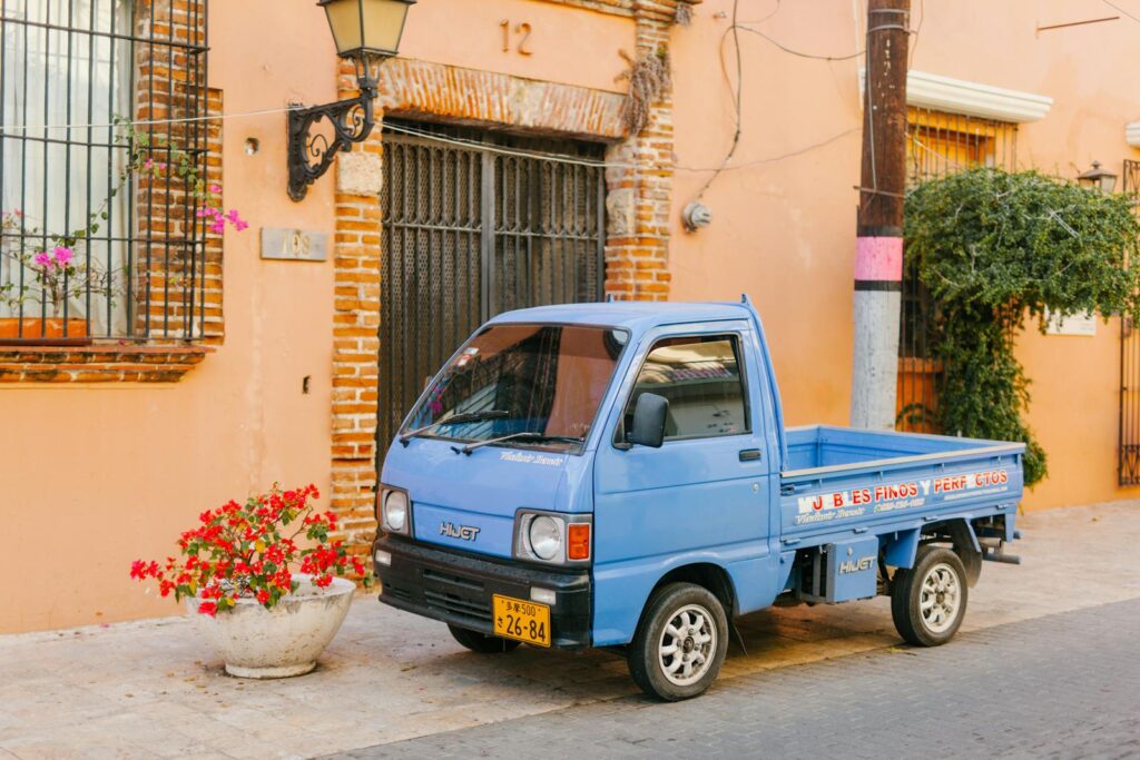 Old mini truck near urban roadway and house facade