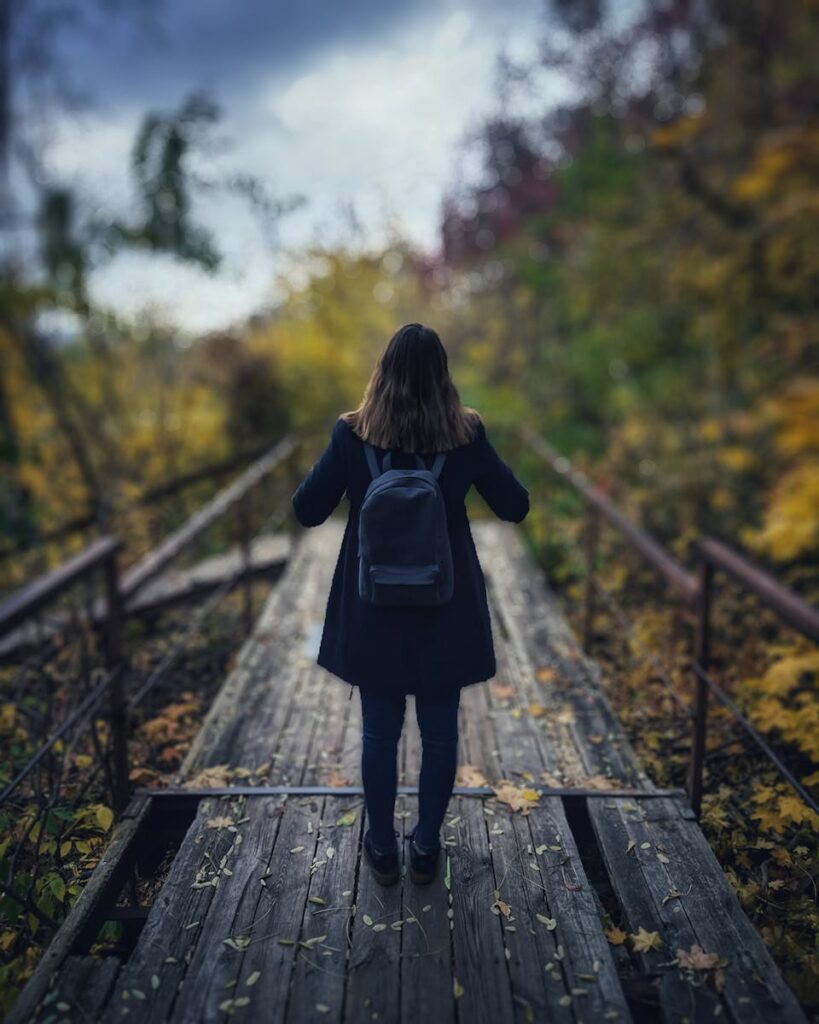 Selective Focus Photography of Woman Wearing Black Overcoat Standing on Wooden Bridge