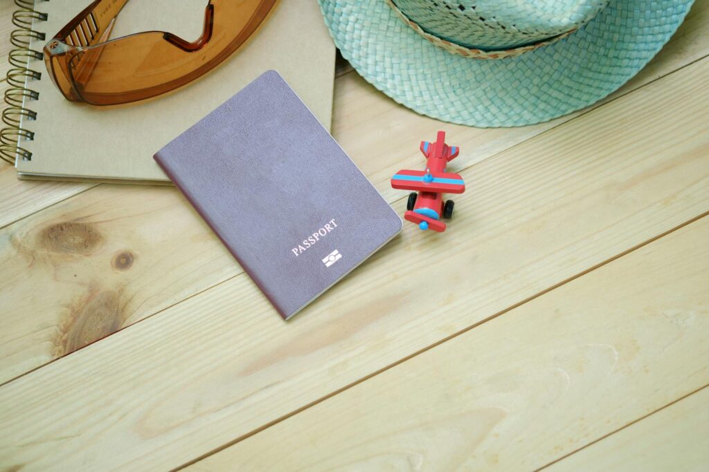 Gray Passport on Brown Board Beside Red Plane Toy